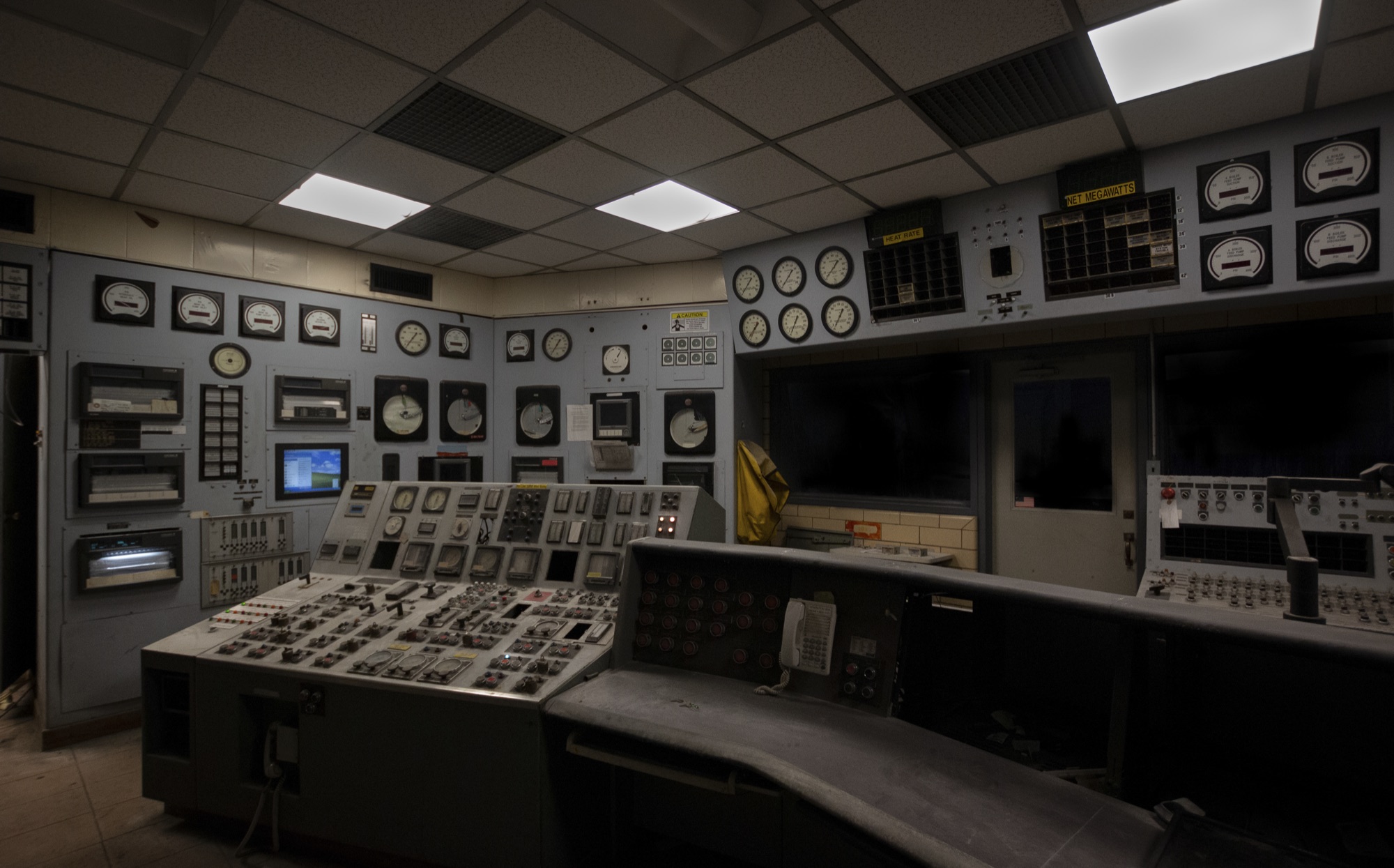 An abandoned control room, banks of dials, gauges and switches wrapping around a curved operator desk