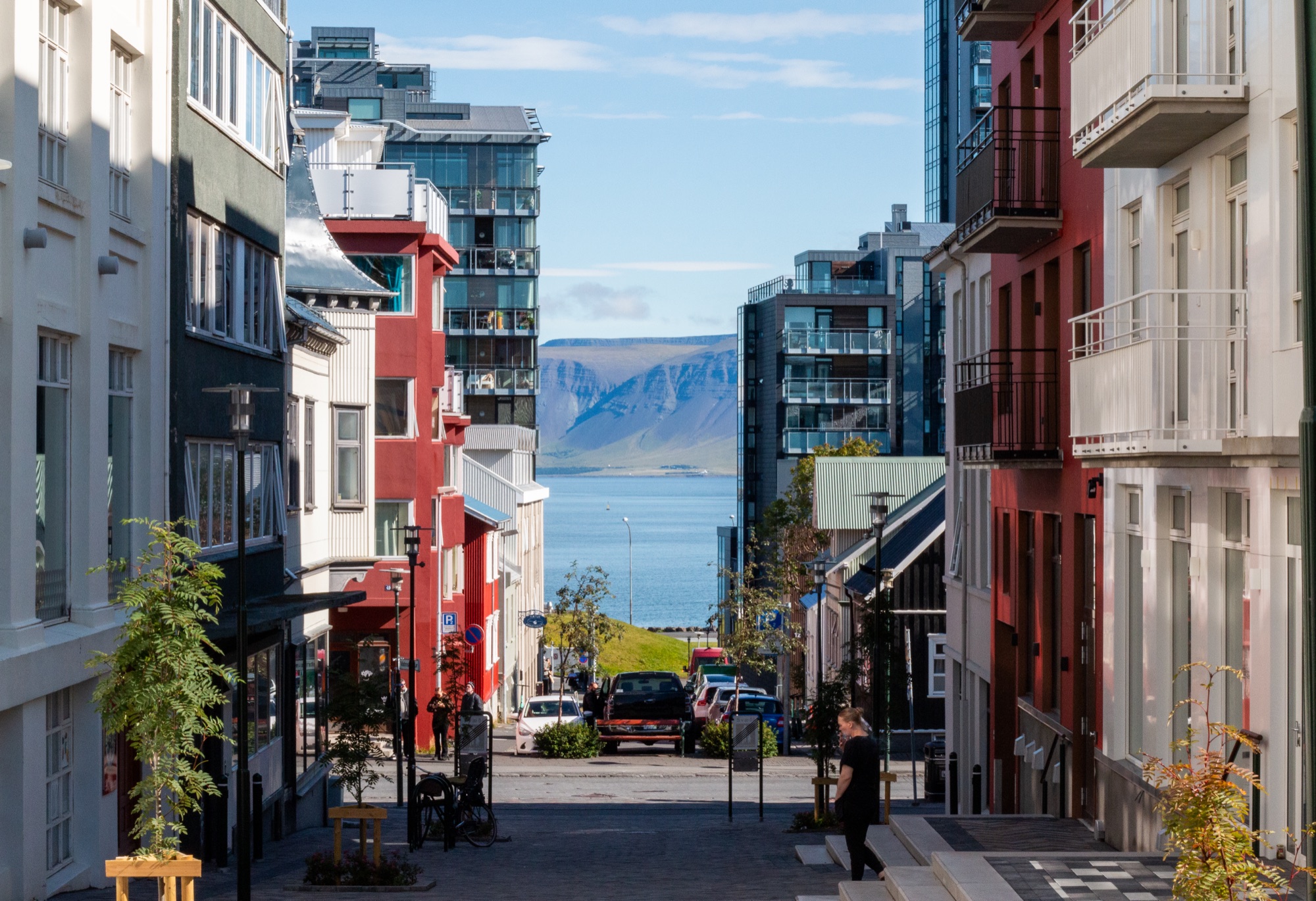 A sloping Reykjavik street lined with brightly painted buildings, framing the bay and a flat-topped mountain beyond