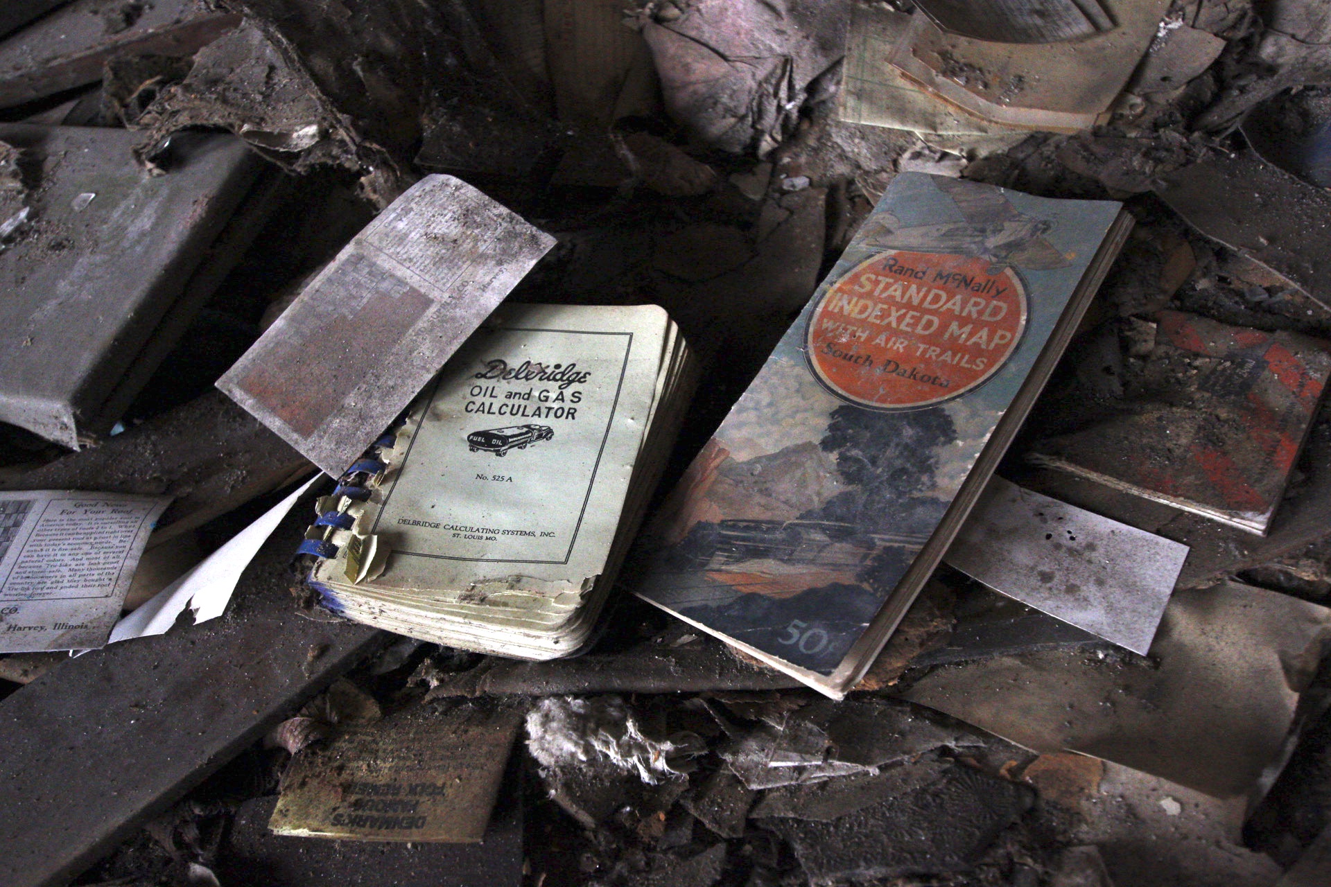 Water-damaged books strewn across a debris-covered floor, an oil and gas calculator and a folded road map among them