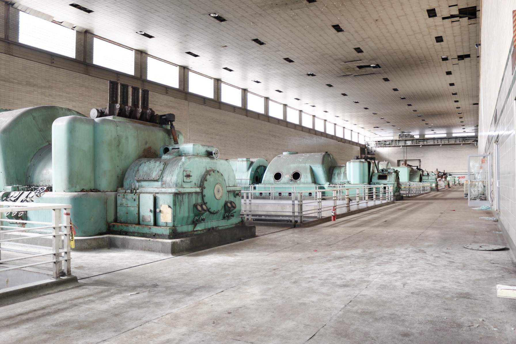 A row of mint-green generators receding down a long turbine hall lit by clerestory windows